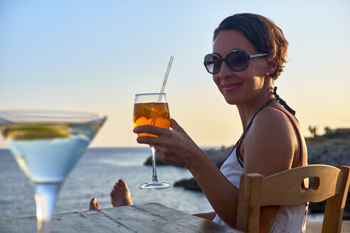 Italien, Santa Caterina, Porträt einer entspannten Frau, die bei Sonnenuntergang mit einem Glas Spritz anstößt - DIKF00274