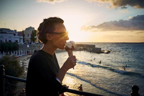 Italien, Santa Maria al Bagno, Frau isst Eiswaffel bei Gegenlicht, lizenzfreies Stockfoto