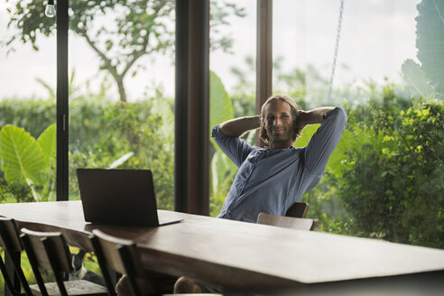 Gut aussehender Mann mit Laptop, der an einem modernen Holztisch in einem modernen Designhaus sitzt - SBOF00811