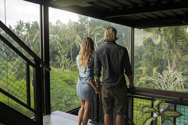 Couple looking at stunning view through glass facade in contemporary design house surrounded by lush tropical garden - SBOF00818