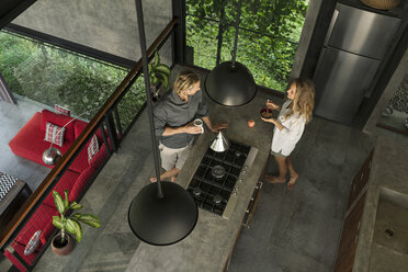 Draufsicht auf ein Paar in einer modernen Design-Küche mit Glasfassade, umgeben von einem üppigen Garten - SBOF00832