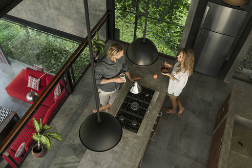 Top view of couple standing in modern design kitchen with glass facade surrounded by lush garden - SBOF00832