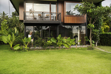 Garden view of couple standing in modern design house surrounded by lush tropical garden - SBOF00843