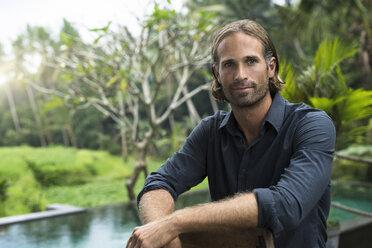 Portrait of handsome man in front of swimming pool and stunning tropical garden - SBOF00851