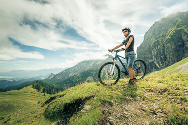 Germany, Bavaria, Pfronten, woman with mountain bike on alpine meadow near Aggenstein - PNPF00025