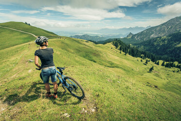 Deutschland, Bayern, Pfronten, Frau mit Mountainbike auf Almwiese bei Aggenstein - PNPF00026