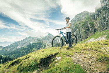 Germany, Bavaria, Pfronten, smiling teenage girl with mountain bike on alpine meadow near Aggenstein - PNPF00029