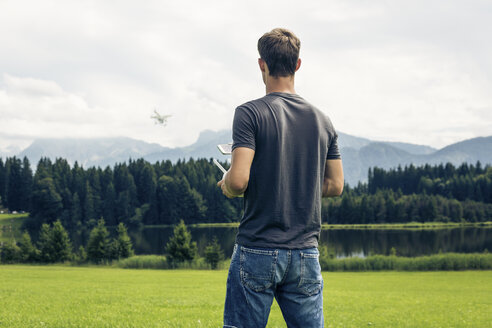 Deutschland, Bayern, Pfronten, junger Mann fliegt seine Drohne am Seeufer - PNPF00033