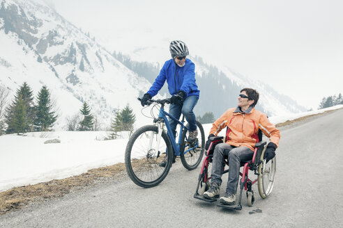 Austria, Damuels, senior couple with bike and wheelchair enjoying a winter day - PNPF00042