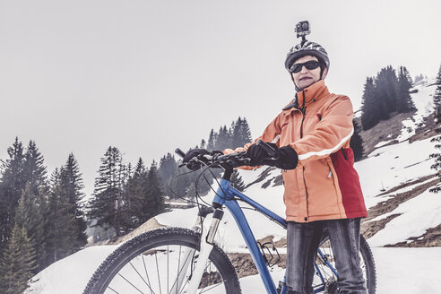 Austria, Damuels, woman with mountain bike and action cam in winter landscape - PNPF00043