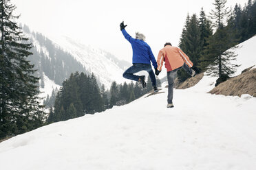 Österreich, Damuels, glückliches Seniorenpaar beim Springen in Winterlandschaft - PNPF00044