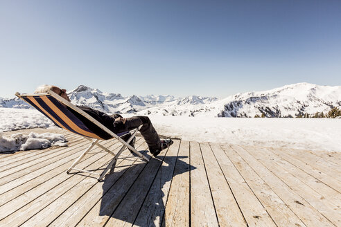 Österreich, Damuels, älterer Mann im Liegestuhl auf Sonnendeck in Winterlandschaft - PNPF00055