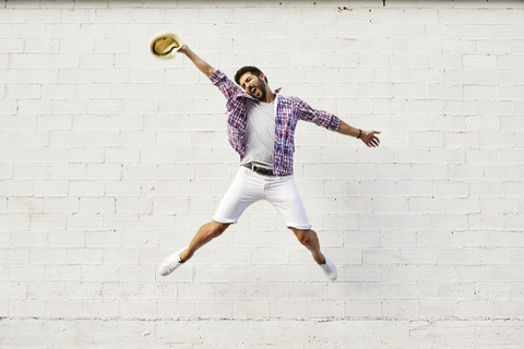 Glücklicher Mann springt in der Luft vor einer weißen Wand, lizenzfreies Stockfoto