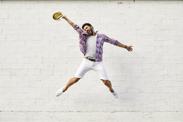 Glücklicher Mann springt in der Luft vor einer weißen Wand - JRFF01446