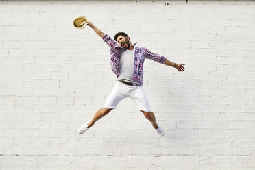 Happy man jumping mid-air in front of white wall - JRFF01446