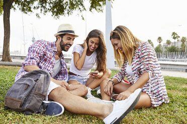 Drei glückliche Freunde sitzen im Park und teilen ihr Smartphone - JRFF01455