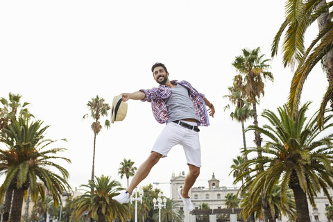 Spain, Barcelona, happy man jumping mid-air surrounded by palm trees stock photo