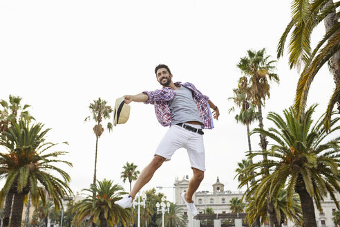 Spain, Barcelona, happy man jumping mid-air surrounded by palm trees - JRFF01463