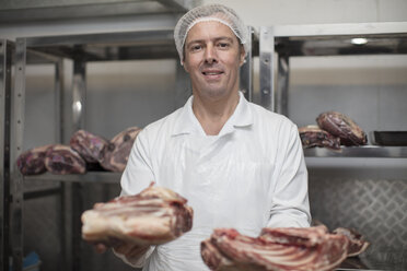 Portrait of smiling butcher holding meat - ZEF14624