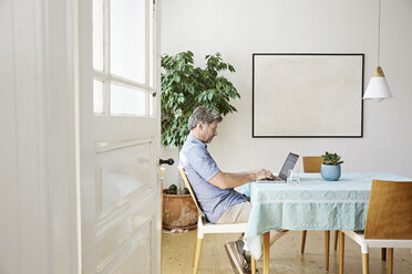 Mature man at home sitting at table, using laptop - PDF01284