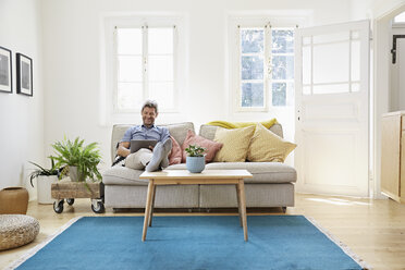 Man sitting on couch at home, using digital tablet - PDF01298