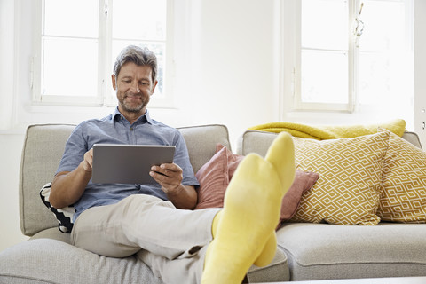 Mann sitzt zu Hause auf der Couch und benutzt ein digitales Tablet, lizenzfreies Stockfoto