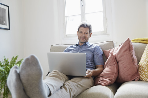 Mann sitzt zu Hause auf der Couch und benutzt einen Laptop, lizenzfreies Stockfoto