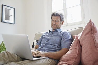 Man sitting on couch at home, using laptop - PDF01305