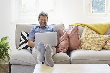 Man sitting on couch at home, using laptop - PDF01309