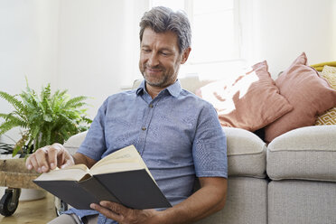 Älterer Mann sitzt zu Hause vor der Couch und liest ein Buch - PDF01312