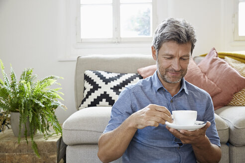Älterer Mann sitzt zu Hause vor der Couch und trinkt Kaffee - PDF01317