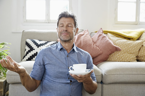 Älterer Mann sitzt zu Hause vor der Couch und trinkt Kaffee, lizenzfreies Stockfoto
