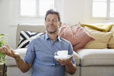Mature man at home sitting in front of couch, drinking coffee - PDF01318