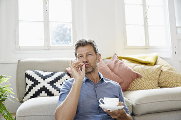 Älterer Mann sitzt zu Hause vor der Couch und trinkt Kaffee - PDF01319