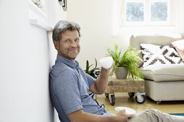 Mature man at home sitting in front of couch, drinking coffee - PDF01323