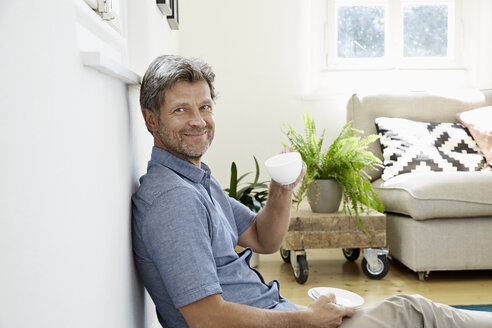 Älterer Mann sitzt zu Hause vor der Couch und trinkt Kaffee - PDF01323