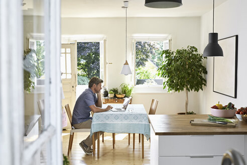 Mature man sitting in his dining room, using laptop - PDF01334