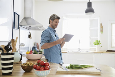 Mature man in his kitchen reading recipe on his digital tablet - PDF01343