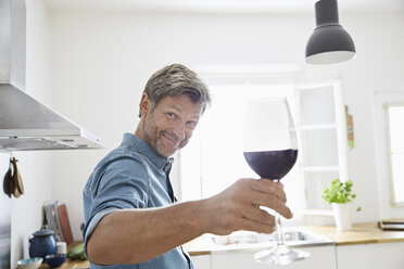 Man in kitchen toasting with glass of red wine - PDF01345