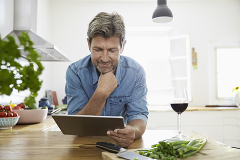 Mature man in his kitchen reading recipe on his digital tablet stock photo