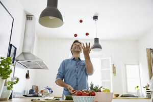 Älterer Mann steht in der Küche und jongliert mit Tomaten - PDF01354