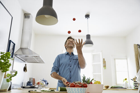 Mature man standing in kitchen, juggling with tomatoes - PDF01354