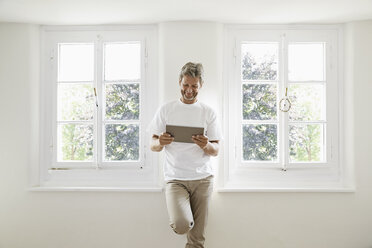 Mature man standing at window using digital tablet - PDF01371