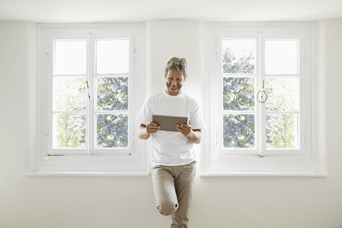 Älterer Mann steht am Fenster und benutzt ein digitales Tablet - PDF01371