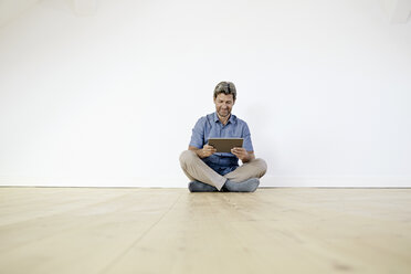 Älterer Mann, der in einem leeren Raum auf dem Boden sitzt und ein digitales Tablet benutzt - PDF01386