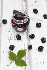 Glass of homemade blackberry jam, blackberries and leaf on wood - LVF06290