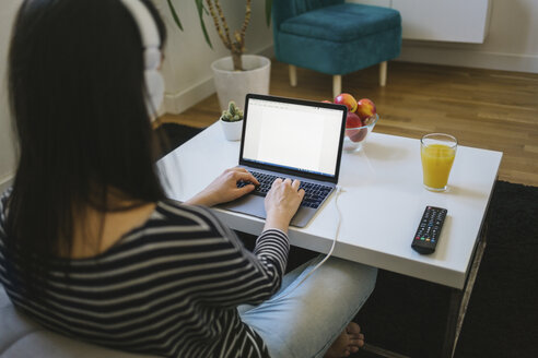 Young woman using laptop and headphones at home - MOMF00254