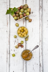 Cardboard box of gooseberries and jars of gooseberry jam and preserved gooseberries on wood - LVF06298