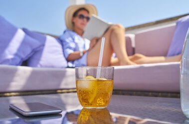 Glass of Crodino, smartphone and woman relaxing on sun deck in background - DIKF00288