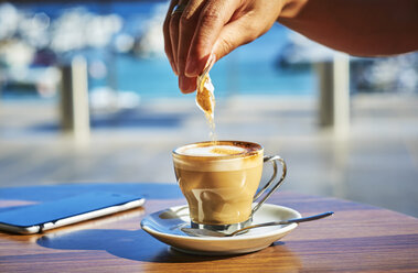 Nahaufnahme einer Frauenhand, die Zucker in ein Glas Espresso Macchiato gießt - DIKF00291